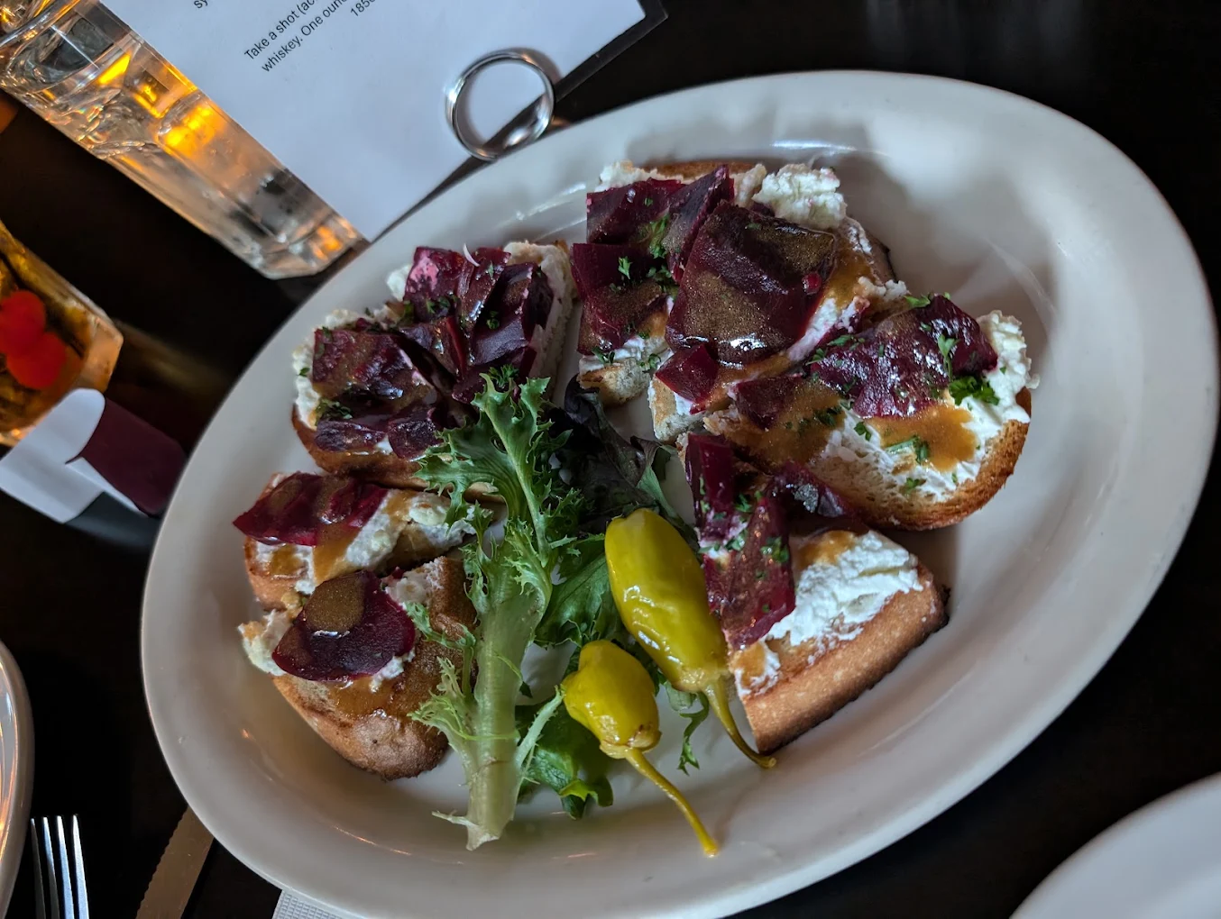 Bruschetta topped with greens, cured meat and peppers