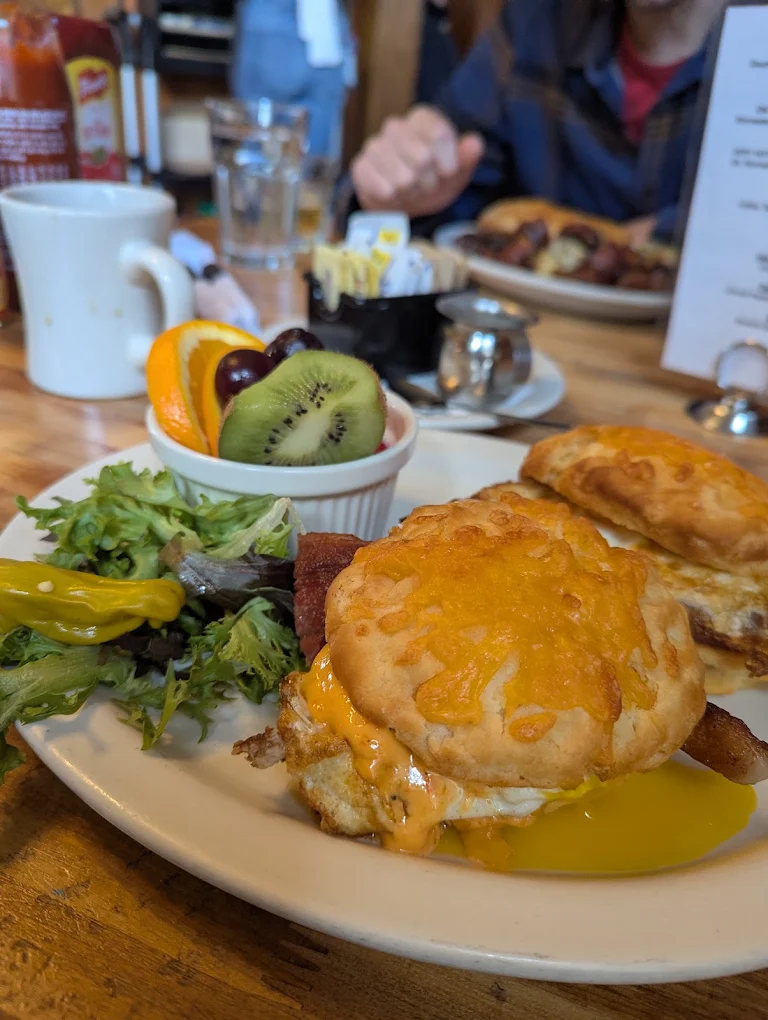 A burger with melted cheese, greens and a side of fruit